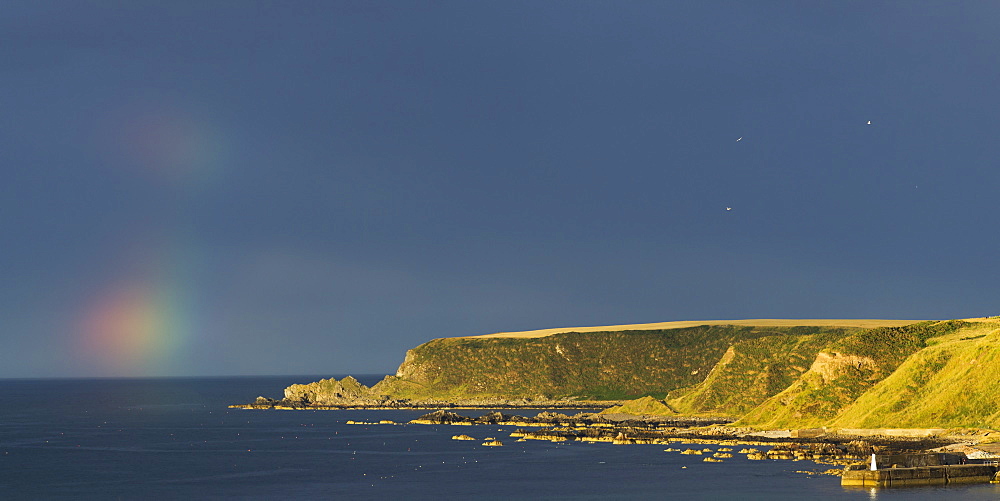 Traces Of A Rainbow In The Sky In The Distance Over The Ocean With Cliffs Along The Coastline, Cullen, Moray, Scotland