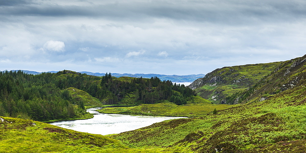 A River Flowing Into A Pond Surrounded By Lush Grass And Forest In The Highlands, Scotland