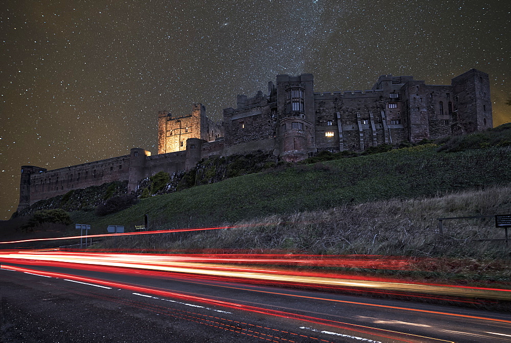 Light Trails On A Road And A Star Filled Sky Over Bamburgh Castle At Nighttime, Bamburgh, Northumberland, England