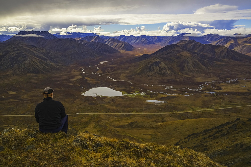 Man Stitting On A Look Out Overlooking The Blackstone Valley, Along The Dempster Highway, Yukon, Canada