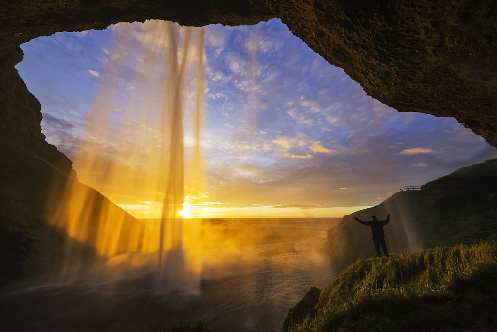 Man Standing Behind The Waterfall Known As Seljandafoss Along The Southern Coast Of Iceland, Iceland