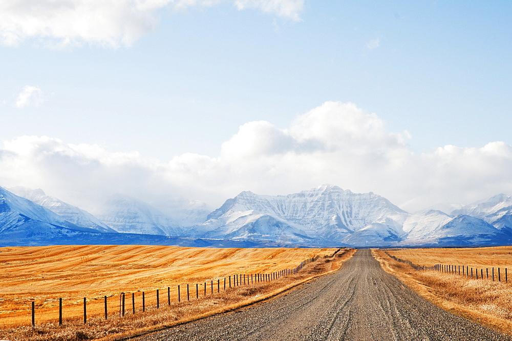 Gravel Road Between Farm Fields And Rocky Mountains In The Distance, Pincher Creek, Alberta, Canada