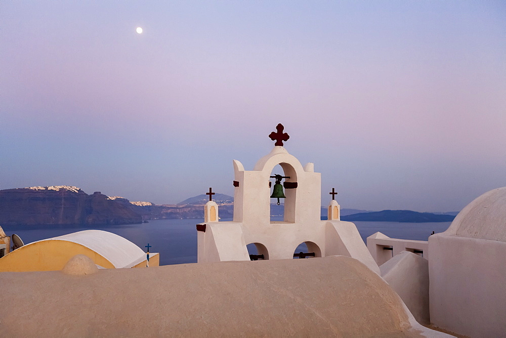 Orthodox Church With Bell And A Moon High In The Sky At Dusk, Oia, Santorini, Greece