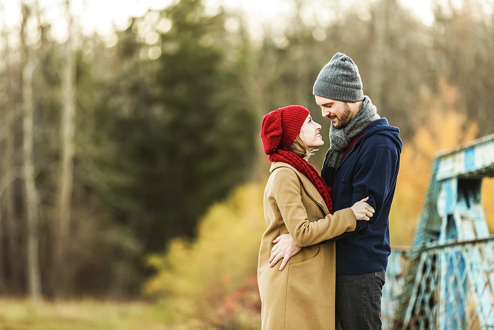 A Young Couple Embracing Each Other And Looking Into Each Other's Eyes On A Bridge In A City Park In Autumn, Edmonton, Alberta, Canada