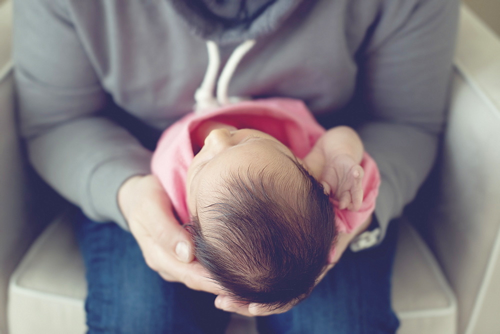 An Adult Holding A Newborn Baby While Sitting In A White Chair, Toronto, Ontario, Canada