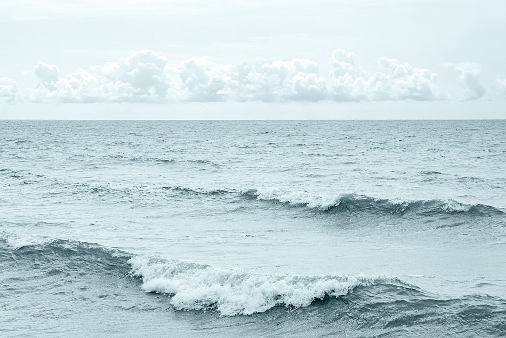 Black and white image of waves diagonal to the image and a band of small cumulus clouds floating right above the horizon, Ontario, Canada