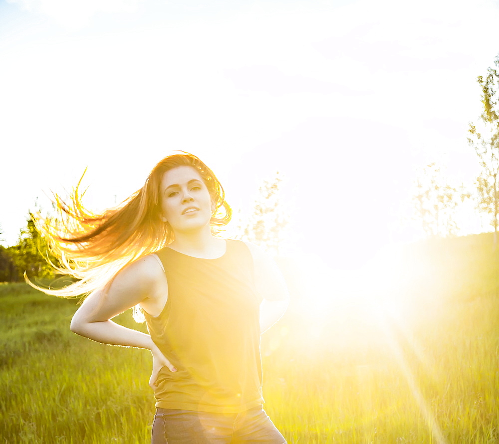 Portrait of a young woman with long hair blowing behind her and a sun flare glowing beside her, Edmonton, Alberta, Canada