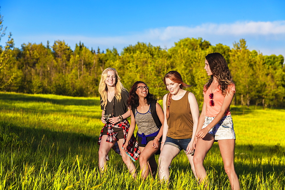 A group of four girlfriends hike together through a field in a park, Edmonton, Alberta, Canada