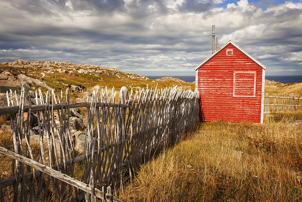 A small red shed beside a wooden picket fence along the coast, Newfoundland, Canada