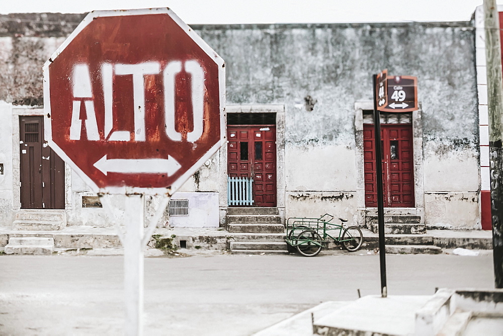 A stop sign with an arrow in Spanish along a street with houses in the background, Cancun, Mexico