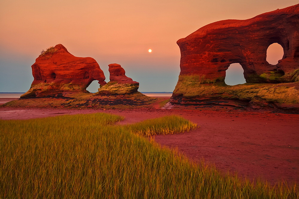 Coastal sea stacks, marsh grass and a full moon at twilight during low tide along the Minas Basin, North Medford, Nova Scotia, Canada