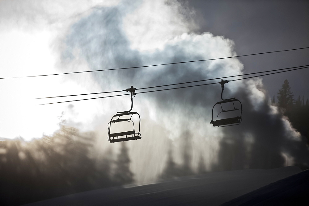 Silhouette of a chairlift on a ski hill with man made snow from snow gun backlit by the sunlight, Copper Mountain Resort, Colorado, United States of America