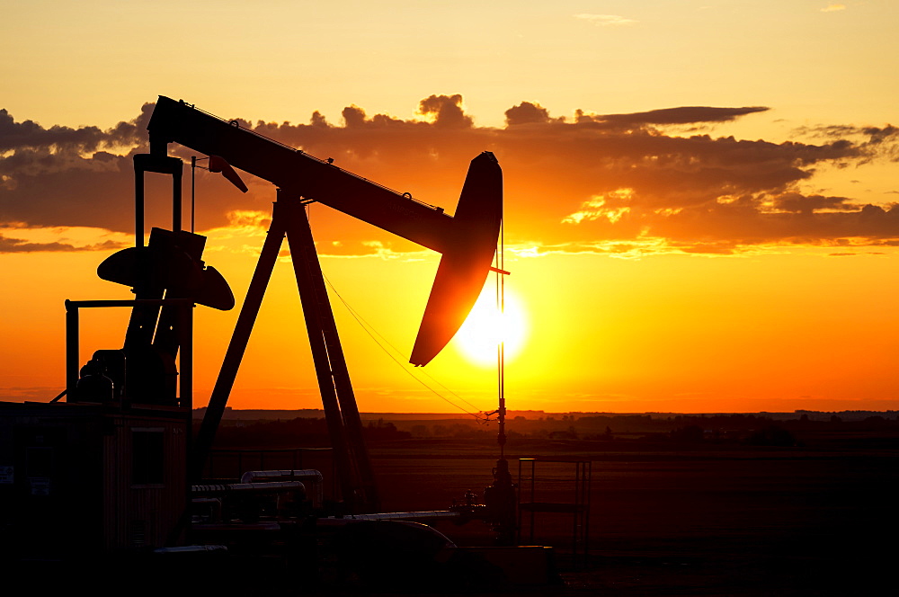 Silhouette Of A Pump Jack At Sunrise With A Colourful Orange Sun, Clouds And Sky, Alberta, Canada