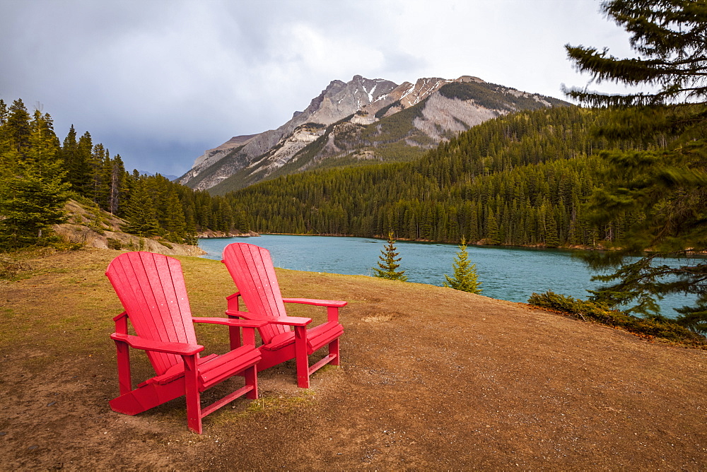 Two Red Adirondack Chairs On A Grassy Hill In Alberta's Mountains And Lakes, Alberta, Canada