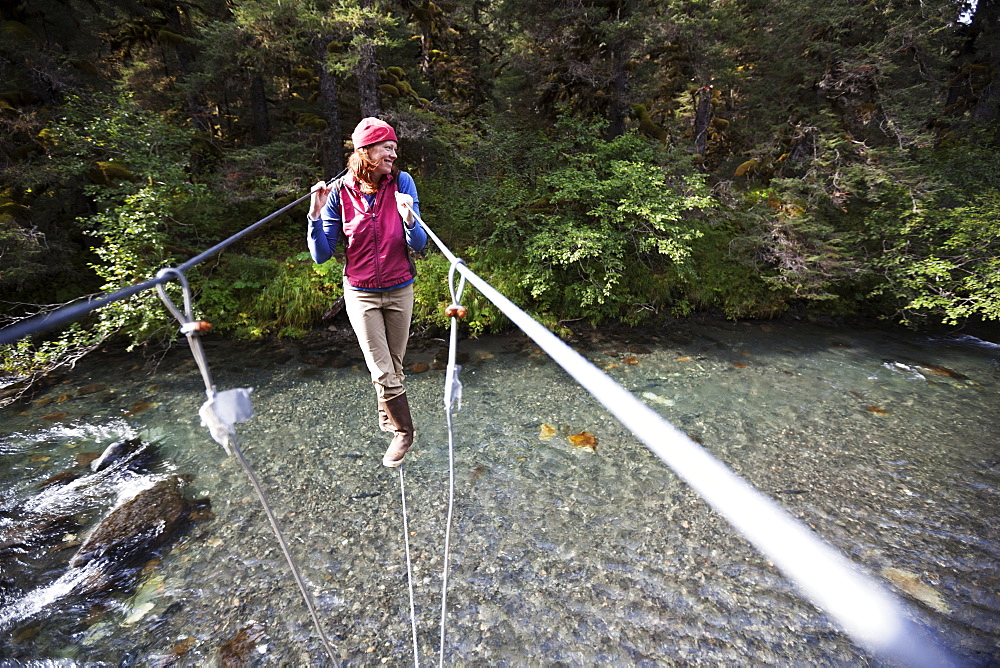 A Woman Walks On A Cable On A Suspension Bridge Over A River, Alaska, United States Of America