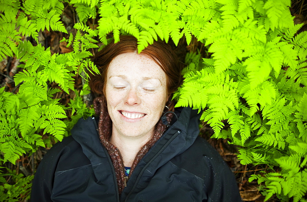 A Woman Lays Her Head On The Forest Floor Among The Bright Green, Lush Ferns, Alaska, United States Of America