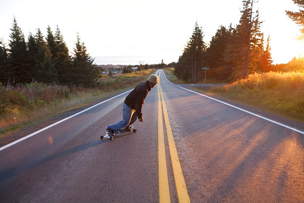 A Young Man Skateboarding Down A Road At Dusk, Homer, Alaska, United States Of America