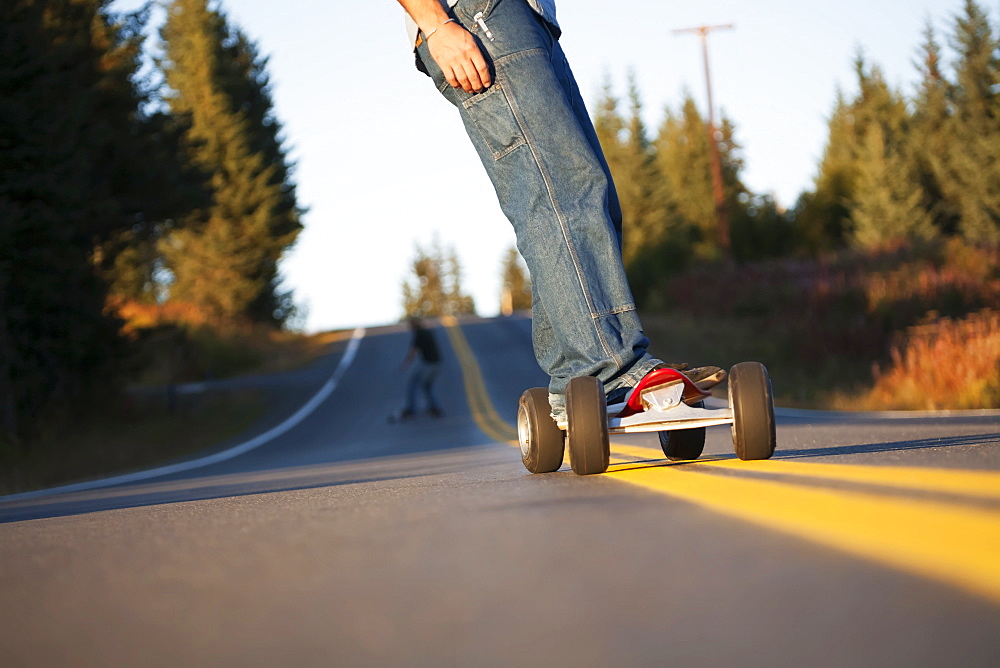 Young Men Skateboarding Down A Road, Homer, Alaska, United States Of America