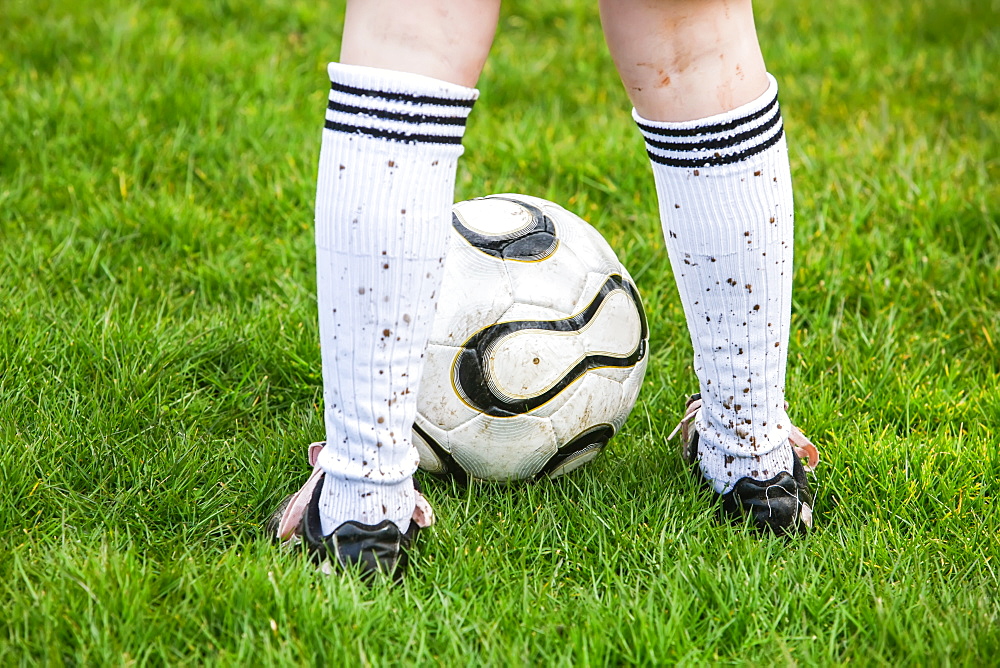 A Soccer Player Standing On A Grass Field With A Soccer Ball And Mud Splashed Socks, Oregon, United States Of America