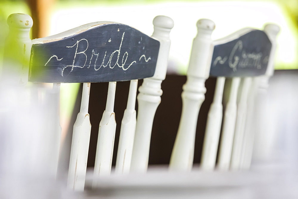 White Wooden Chairs Side By Side With Bride And Groom Written In Chalk On A Chalkboard Finish On The Back