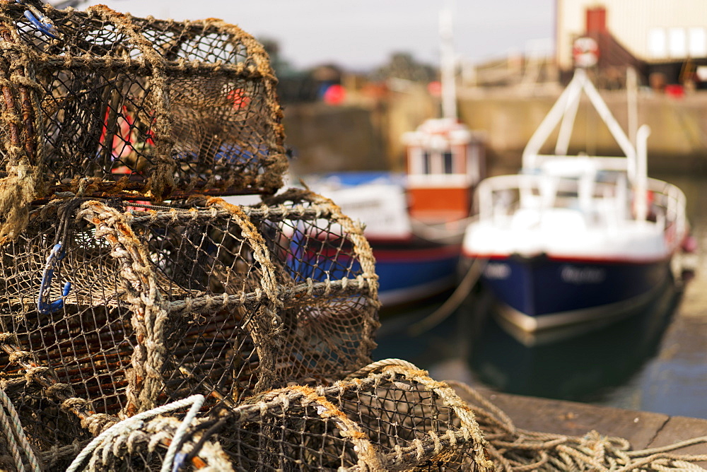 Traps Sitting On The Shore With Fishing Boats Moored In The Background, St. Abbs Head, Scottish Borders, Scotland