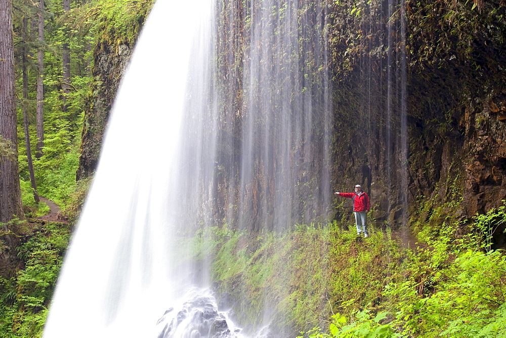 Oregon, United States Of America; A Person Reaching Out To Touch As They Stand Behind North Middle Falls In Silver Falls State Park