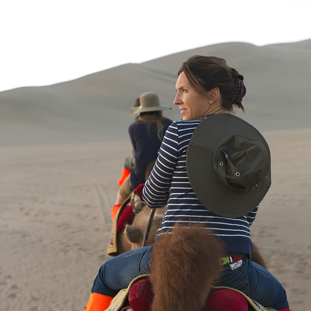 A woman and her daughters riding camels on a desert landscape, Jiuquan gansu china