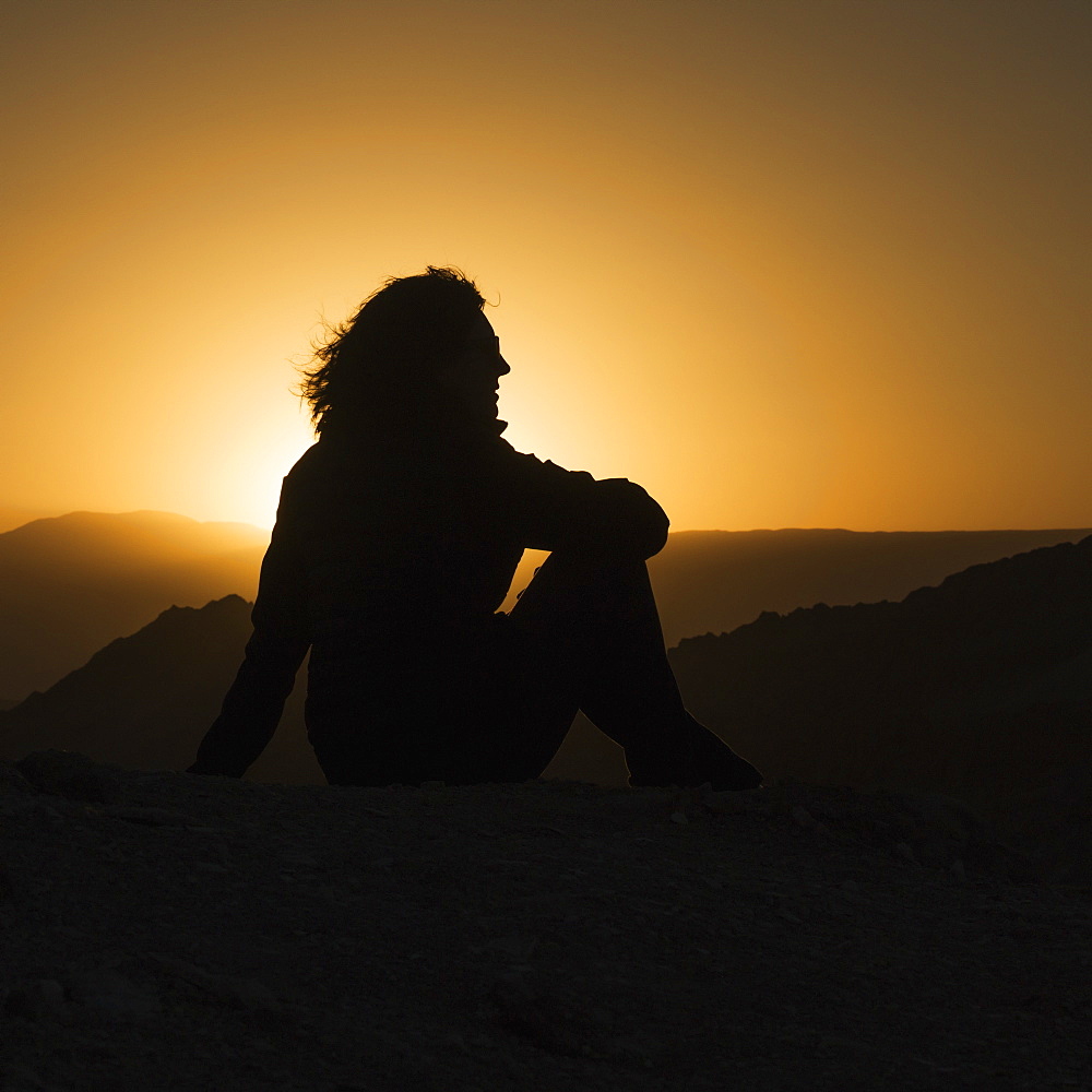 Silhouette Of A Woman Sitting With A View Of The Hilly Landscape Of Valle De La Luna At Sunset, San Pedro De Atacama, Antofagasta Region, Chile