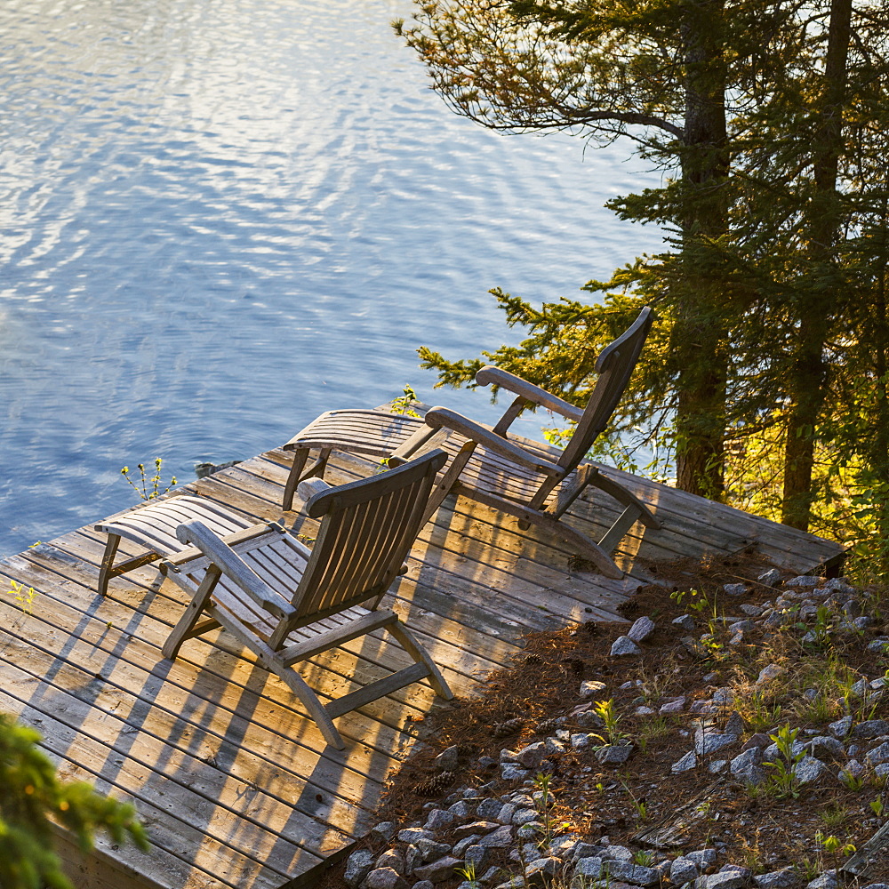 Two Wooden Lounge Chairs On A Dock Looking Out At Lake Of The Woods At Dusk, Ontario, Canada