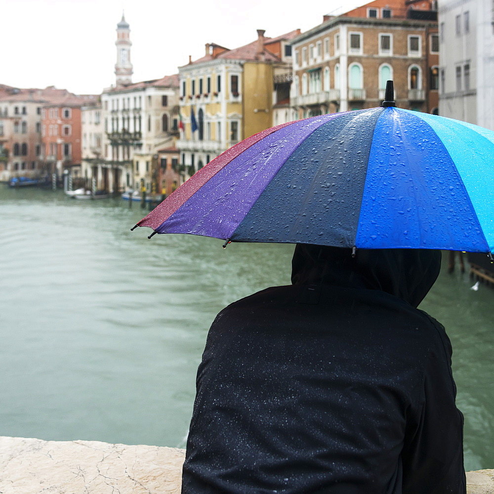 A Person Standing With A Wet, Colourful, Umbrella Looking Out Over A Canal, Venice, Italy