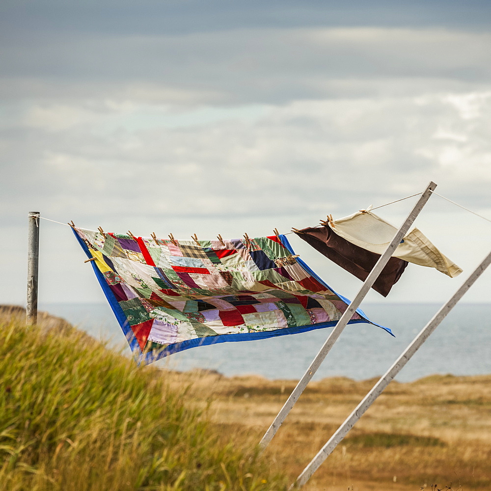 A patchwork blanket and pillow cases hanging on a clothesline with the Atlantic ocean in the background, Newfoundland, Canada