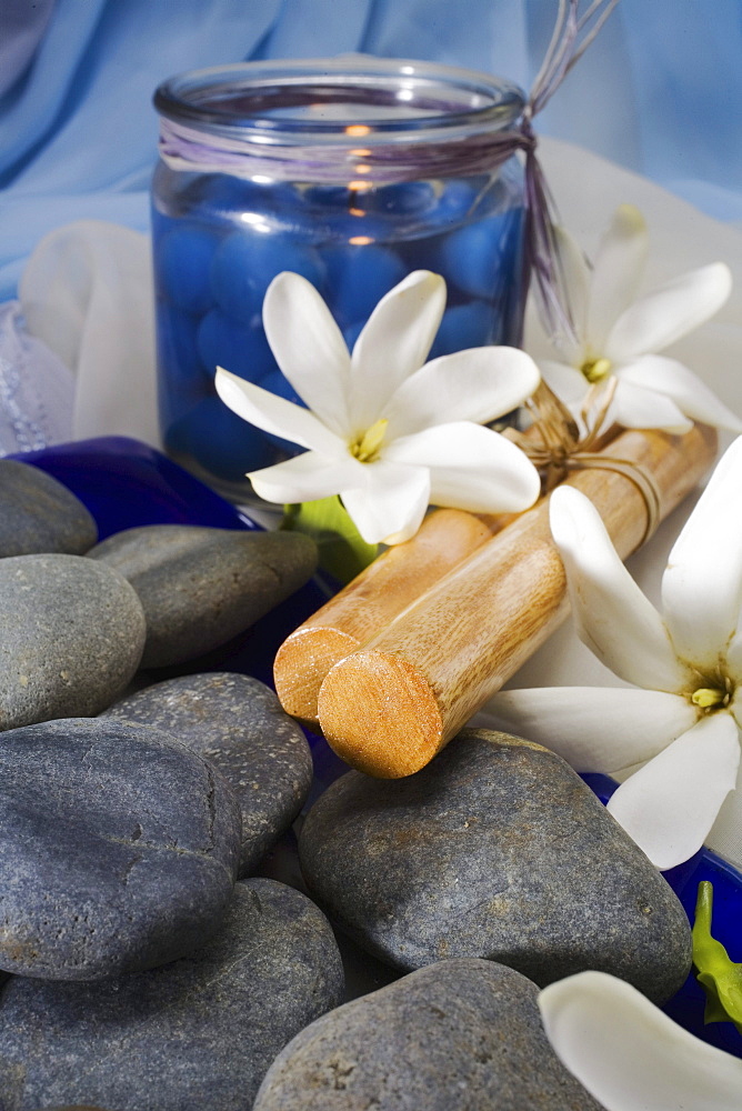 Spa elements, candle, flowers, Hawaiian hula sticks and grey stones.