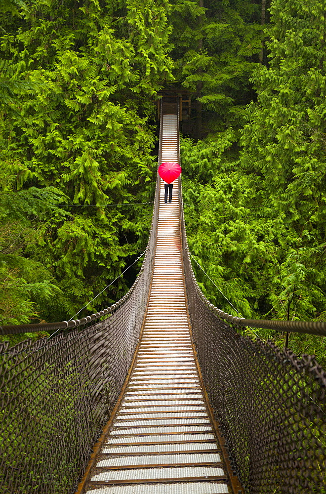 Woman With A Red Heart-Shaped Umbrella Crossing The Lynn Canyon Suspension Bridge, North Vancouver; Vancouver, British Columbia, Canada