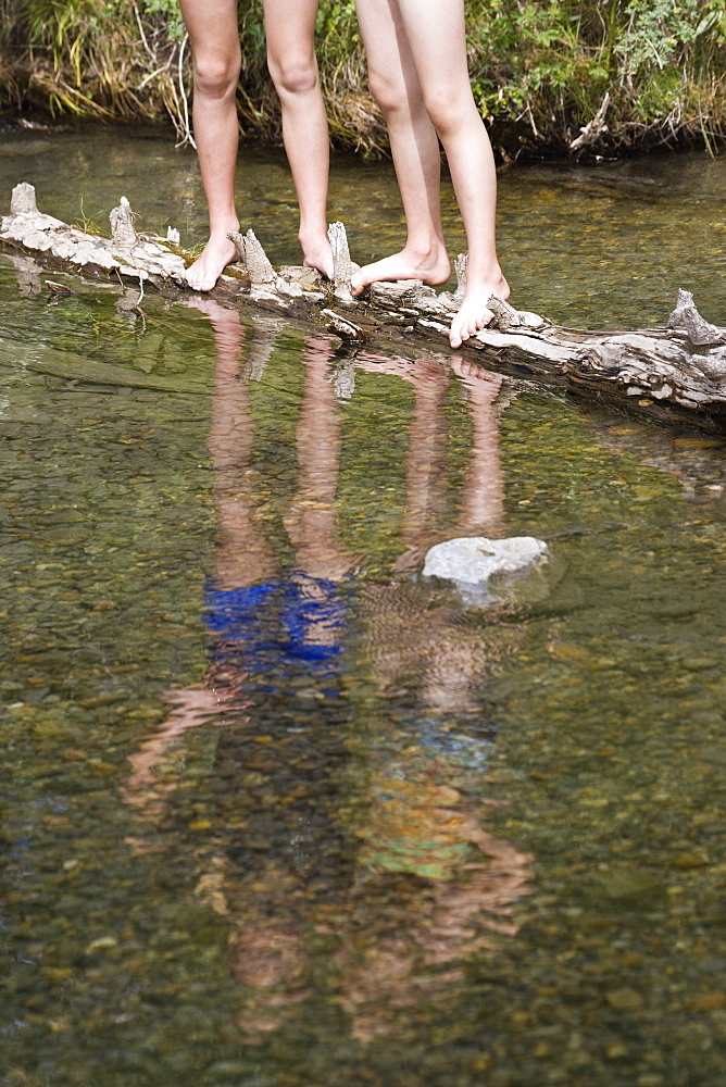 Two Girls Standing On Log In Stream