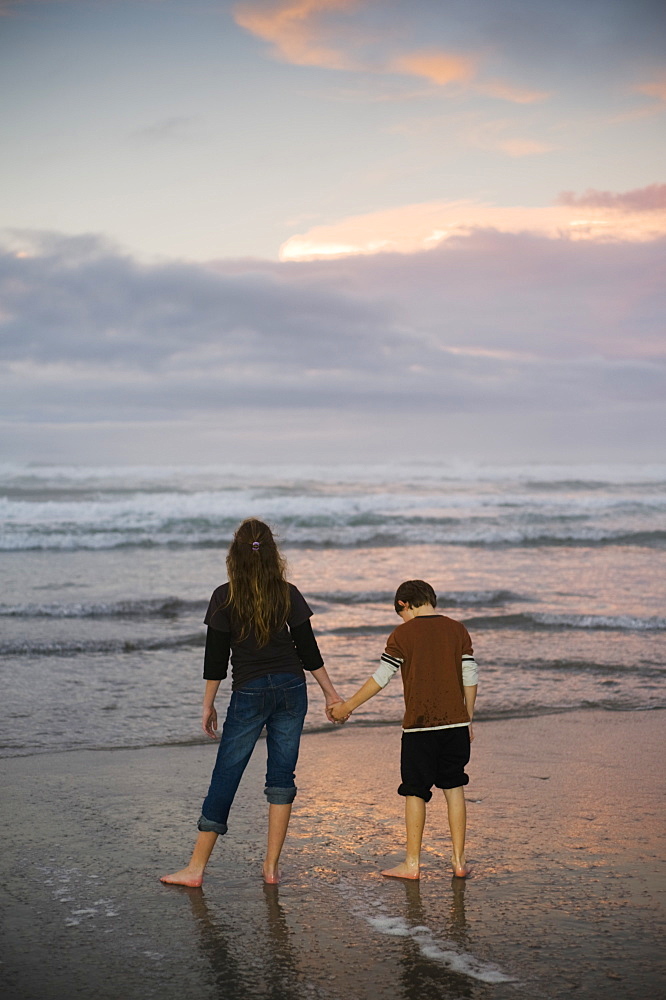 A Mother And Son Hold Hands On A Beach Looking Out At The Water