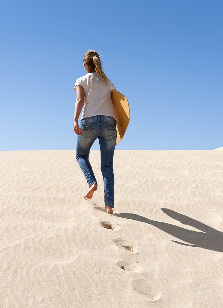 A Young Woman Walks With A Board Over The Punta Paloma Sand Dunes, Tarifa, Cadiz, Andalusia, Spain