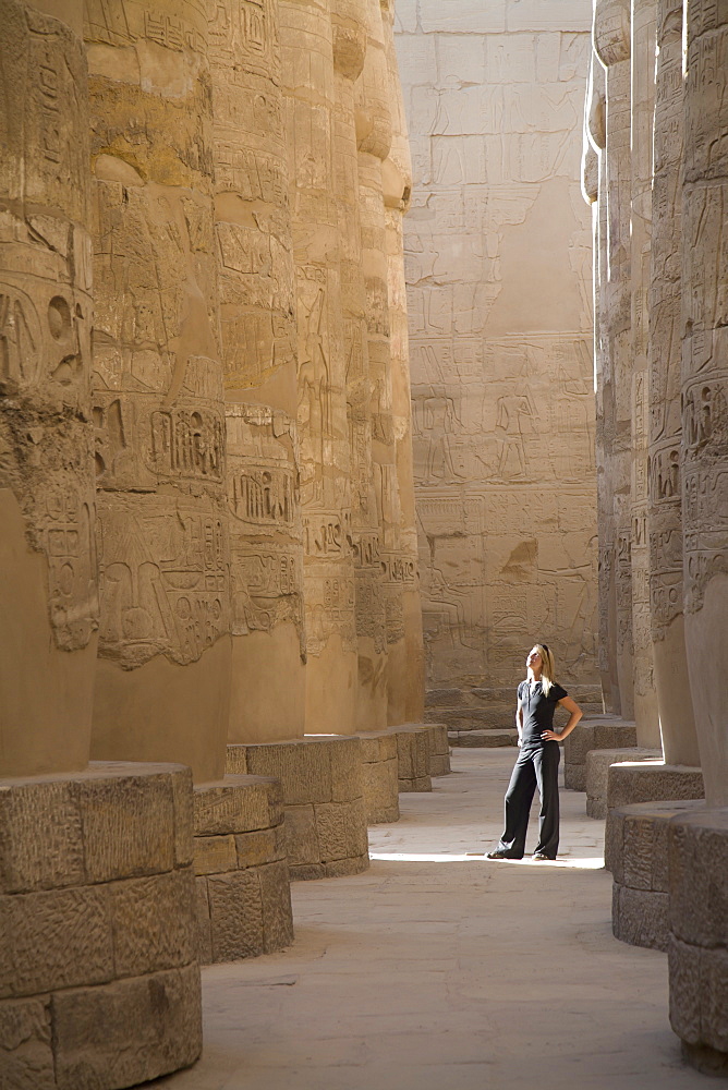 A Woman Tourist Stands At The Base Of The Massive Columns In The Temples Of Karnak On The East Bank Of Luxor Along The Nile River, Luxor, Egypt