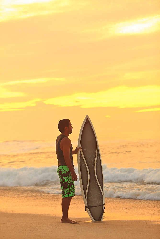 Surfer With His Surfboard At The Water's Edge At Sunset, Baja California Sur, Mexico