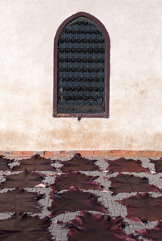 Animal skin mats in a row on the ground facing a wall with a screened window