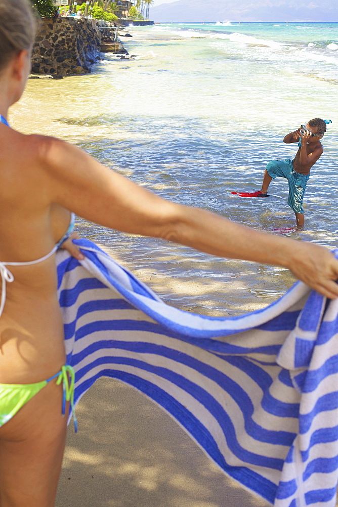 A mother holds a towel out for her son as he comes out of the water with snorkelling gear, Hawaii united states of america