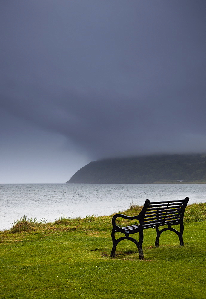 A bench at the water's edge with a dark stormy sky, Moray firth scotland