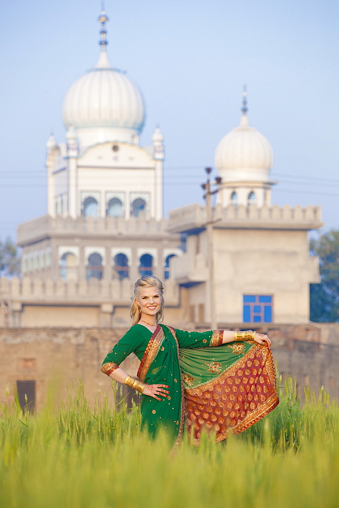 Portrait Of A Blond Woman Wearing A Sari In A Field With A Temple In The Background, Ludhiana, Punjab, India