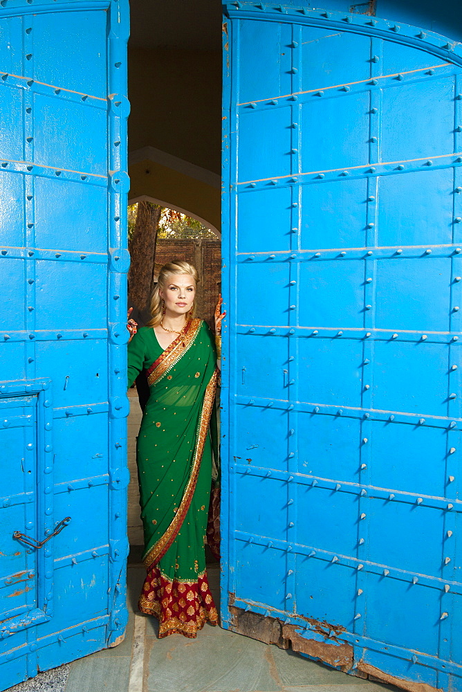 Portrait Of A Blond Woman Wearing A Sari Standing In The Doorway With Large Blue Doors, Ludhiana, Punjab, India