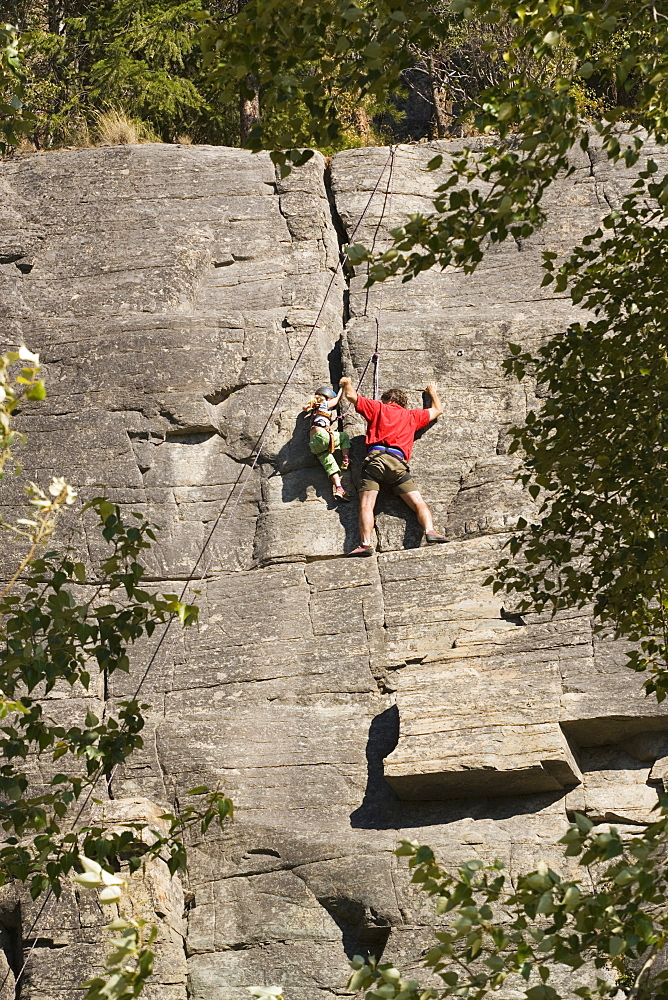 Mid-Age Man Climbing With Daughter (Age 5) Up Granite Cliff At Stone Hills Near Rexford, Montana, Usa