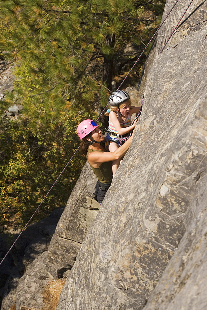 Young Woman Climbing With Daughter (Age 7) Up Granite Cliff At Stone Hills Near Rexford, Montana, Usa