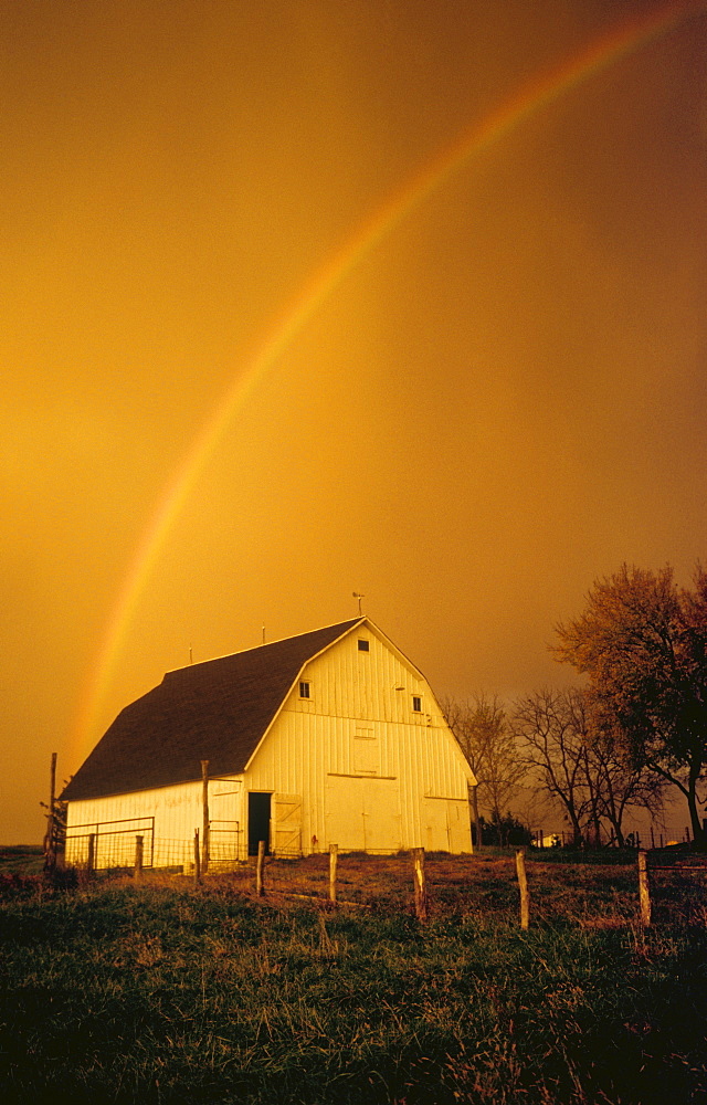 Agriculture - A rainbow arcs over a gambrel roof barn in dramatic stormy light / Northwest Missouri, USA.