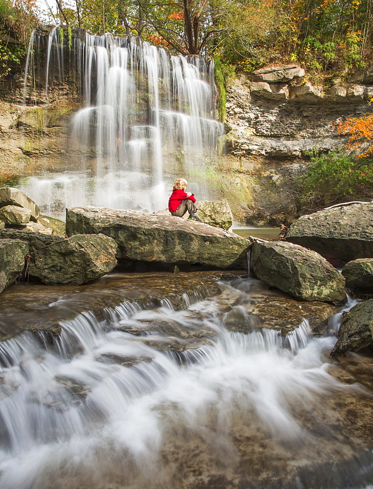 Young Boy Sitting On A Rock Watching The Falls At Rock Glen Conservation Area, Ontario, Canada