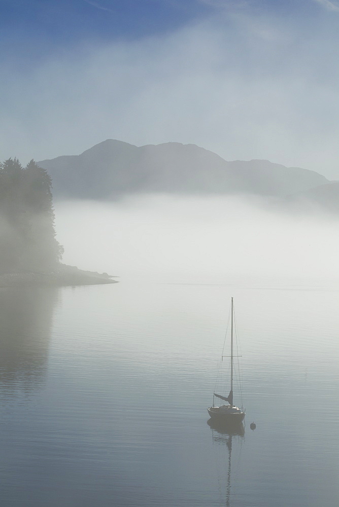 Low Fog And Mist Burn Off Along The Shoreline In Alaska's Inside Passage Where A Sailboat Rests At Anchor In A Small Cove Near Juneau, Alaska. Tongass National Forest.