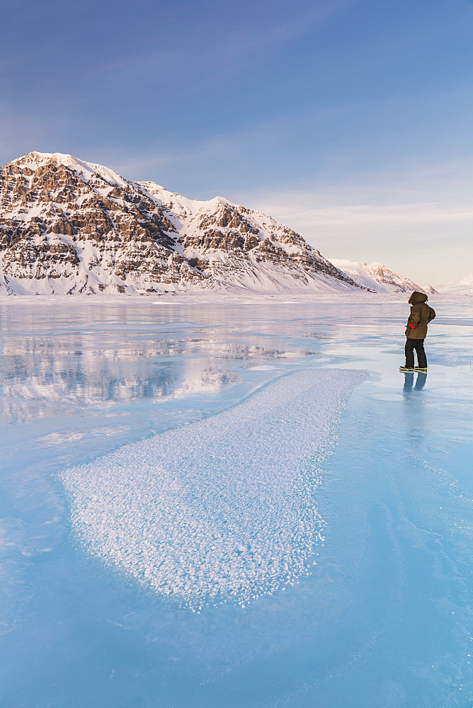 Man In A Parka Standing On Overflow Ice On The Frozen Anaktuvuk River, Hoar Frost Crystals In The Foreground, Napaktualuit Mountain In The Background, Gates Of The Arctic National Park, Alaska, United States Of America