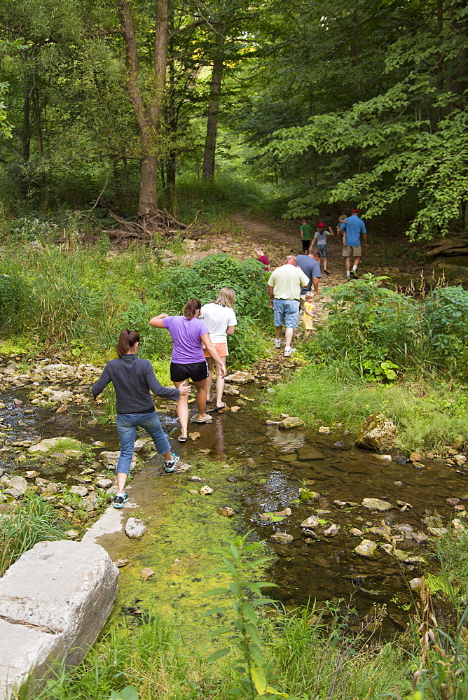 Family Crossing Bear Creek On Hiking Trail Leading To The Ice Cave At Bixby State Preserve, Near Edgewood, Iowa, United States Of America